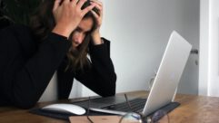 一名女子抱着头看着笔记本电脑屏幕。