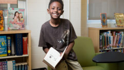 黑人男性中学生与书坐在椅子的手臂,微笑读写课程