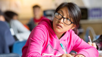 拉美裔女孩写在一本笔记本在教室里看着她的肩膀——对双语教育的文章。