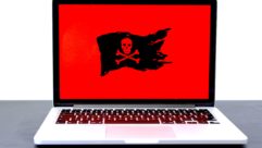 笔记本电脑与黑色头骨和交叉骨在教育网络安全文章红色背景