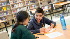一名高中男学生在图书馆的桌子上与一名女老师或同学谈论关于身边同学的文章