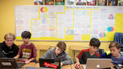 五个小男孩坐在教室的桌子前，一起在笔记本电脑上写一篇关于共同设计的文章
