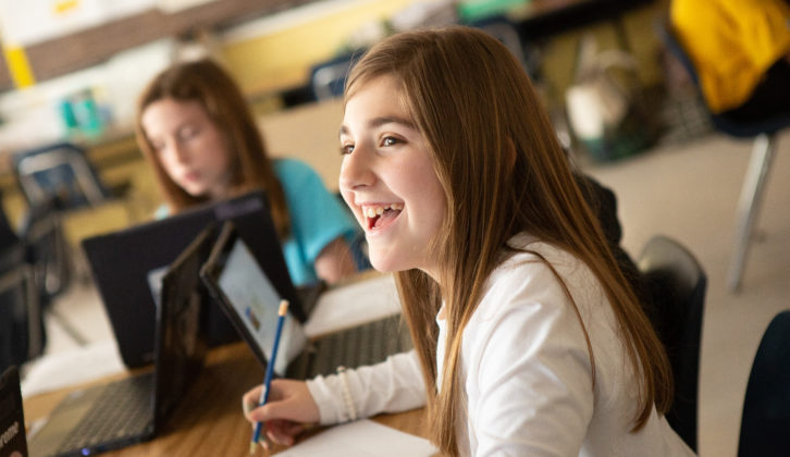 为一篇关于学生选择的文章，一名微笑的中学女学生与其他学生坐在桌子旁