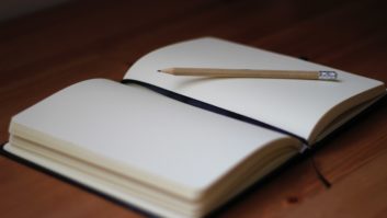 空白日记本，上面放着铅笔，坐在木桌上写一篇关于让“水疗日”充满活力的文章