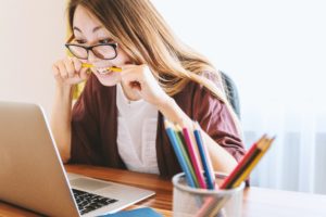 戴眼镜的女孩一边焦虑地咬着铅笔，一边看着笔记本电脑上关于网络安全方法的文章