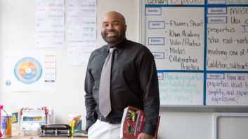黑人男老师拿着书在他身边，微笑着在教室里为老师辅导周期文章