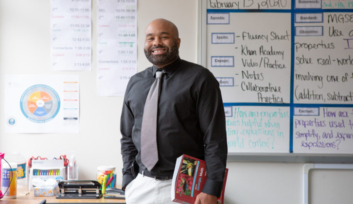 黑人男老师拿着书在他身边，微笑着在教室里为老师辅导周期文章