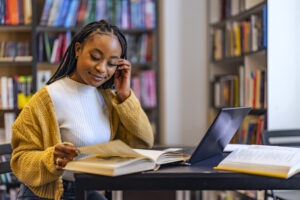 一个黑人女孩在图书馆的桌子上看着笔记本电脑前的书关于在线考试的文章