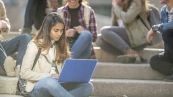 笔记本电脑在前台的女孩坐在台阶的学校与其他学生文章Horace Mann奖