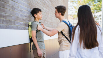 1学校男孩推动另一个靠墙,拿着他的背包肩带在学校女孩手表的文章trauma-informed方法