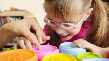 视力不佳的小女孩在玩色彩触觉玩具杯和她的老师作为职业疗法的一部分。文章在职业治疗师短缺