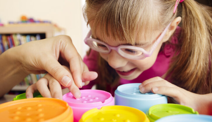 视力不佳的小女孩在玩色彩触觉玩具杯和她的老师作为职业疗法的一部分。文章在职业治疗师短缺