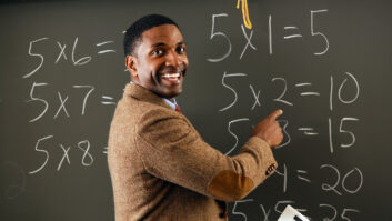 黑人男性教师sportscoat指着黑板的数学方程,面带微笑